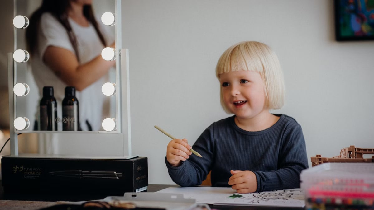A smiling child enjoying drawing indoors with a pencil, sitting at a desk with art supplies.